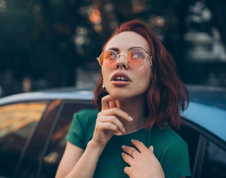 Beautiful fashionable young woman in glasses posing near car